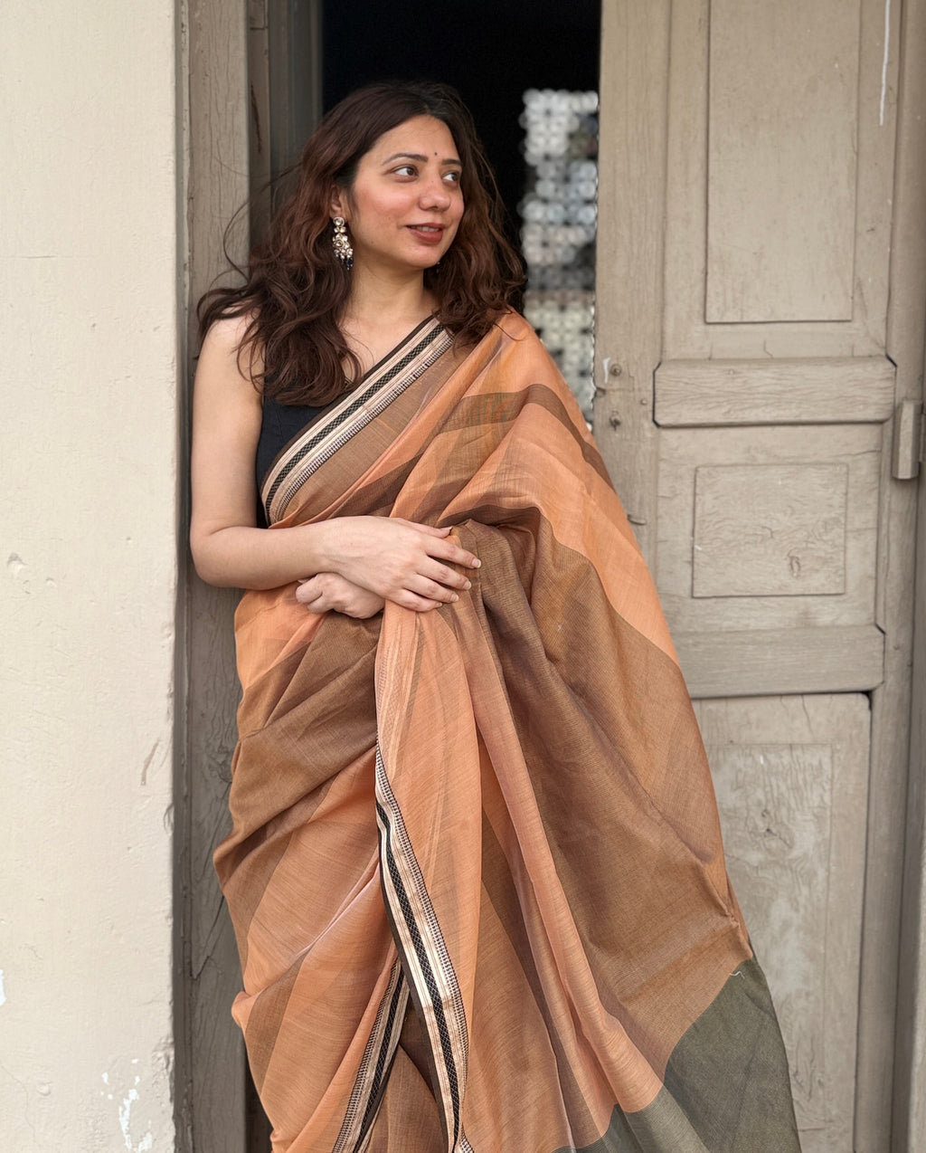 Woman in a brown maheshwari cotton silk saree standing in a doorway