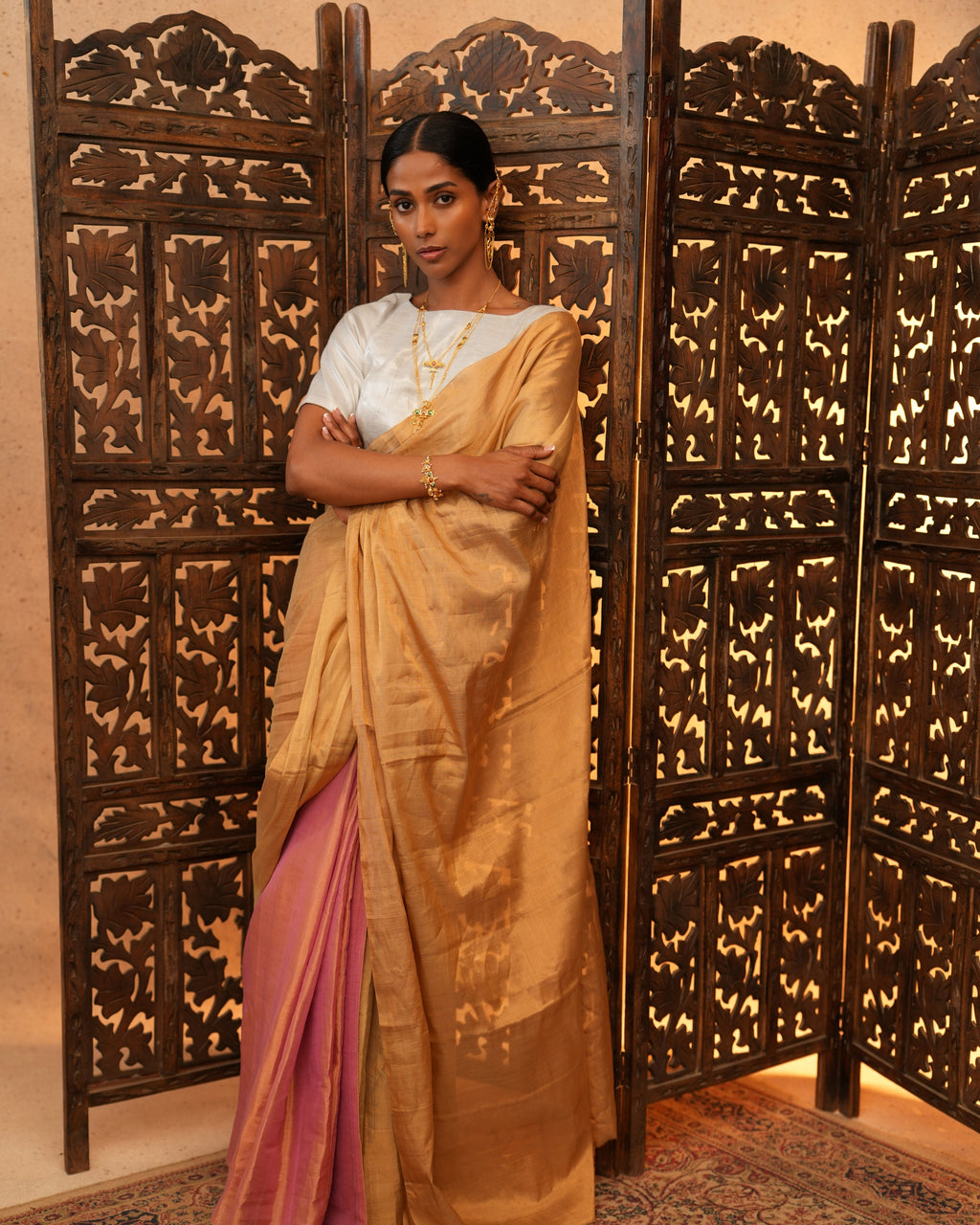 Woman in a traditional chanderi tissue saree standing in front of an ornate wooden screen.