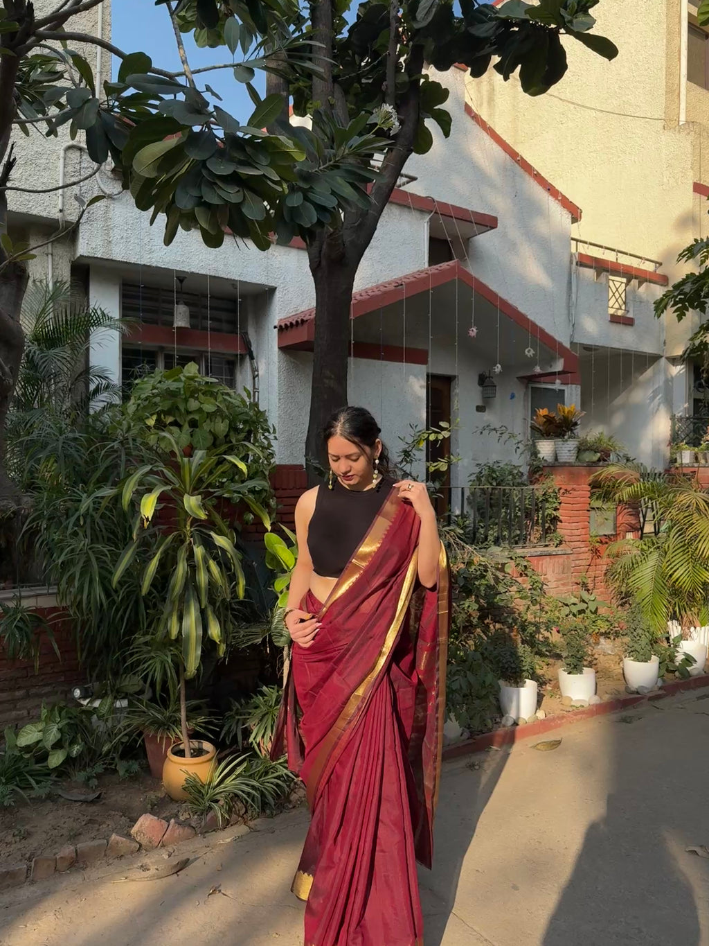 Woman in a red saree standing in a garden with a building in the background