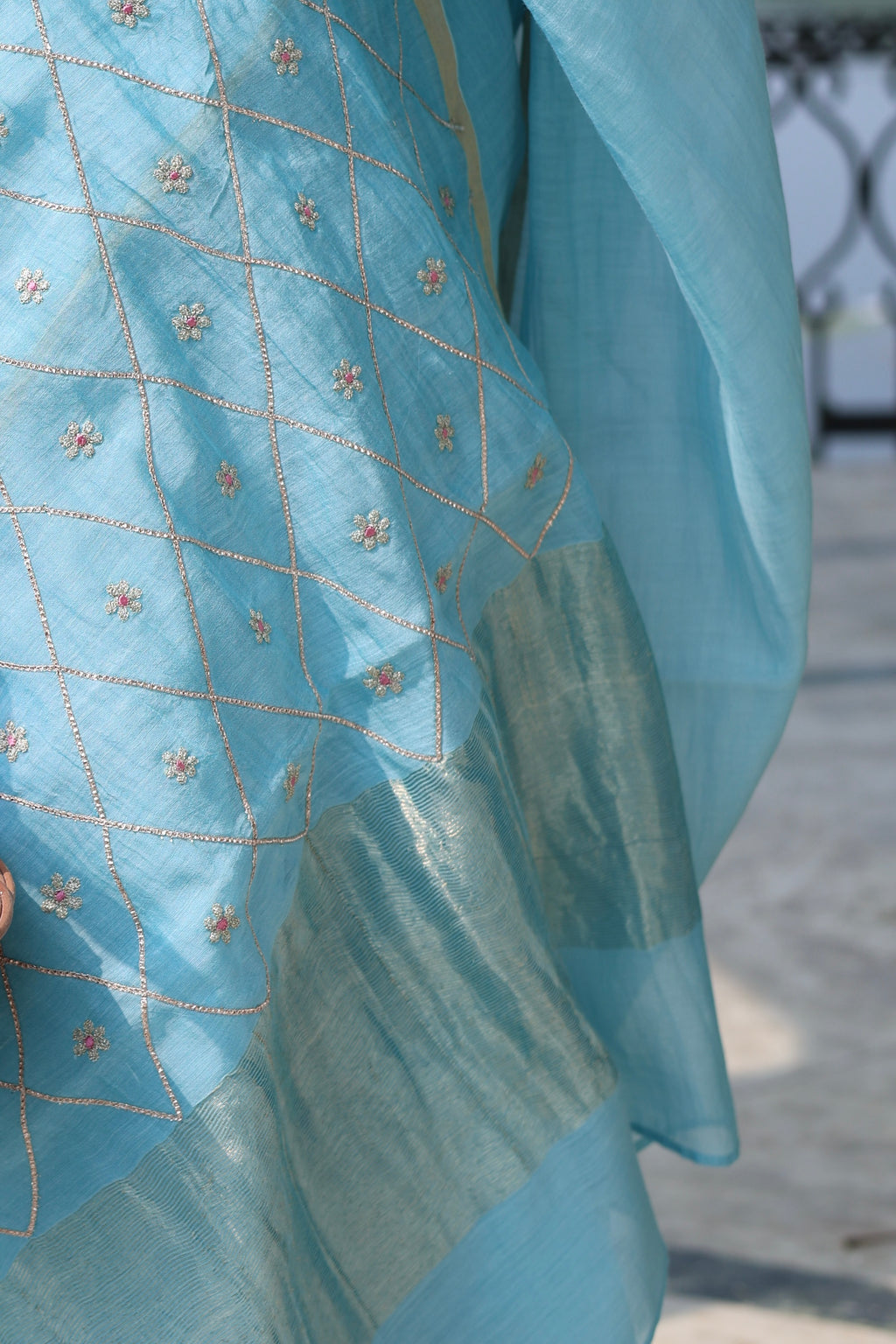 Close-up of a light blue fabric with intricate patterns, possibly a sari or a similar garment.