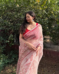 Woman wearing a red and white kota doria cotton patterned saree standing in front of green foliage.