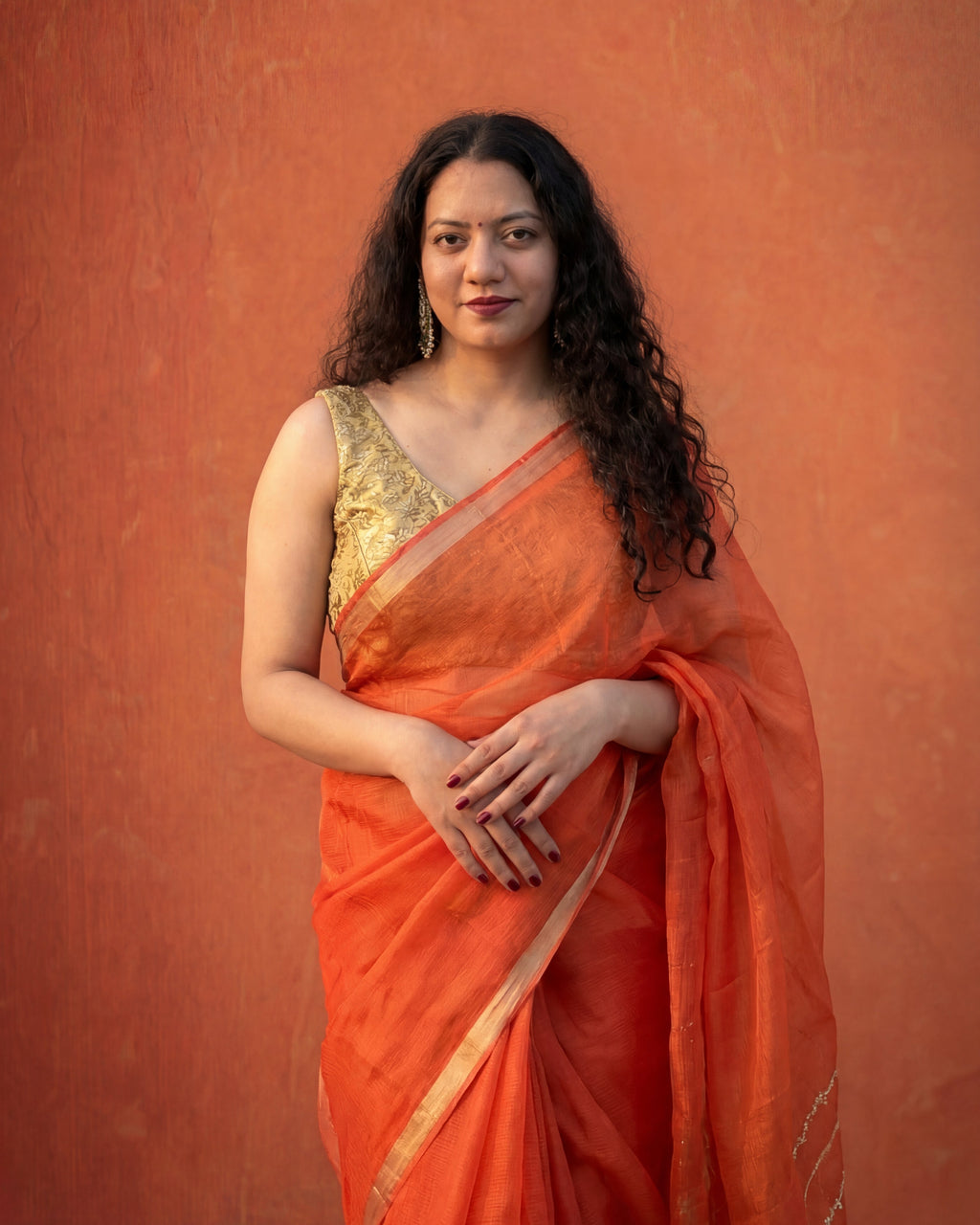 Woman wearing an orange kota silk saree with a gold blouse against an orange background