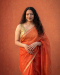Woman wearing an orange kota silk saree with a gold blouse against an orange background