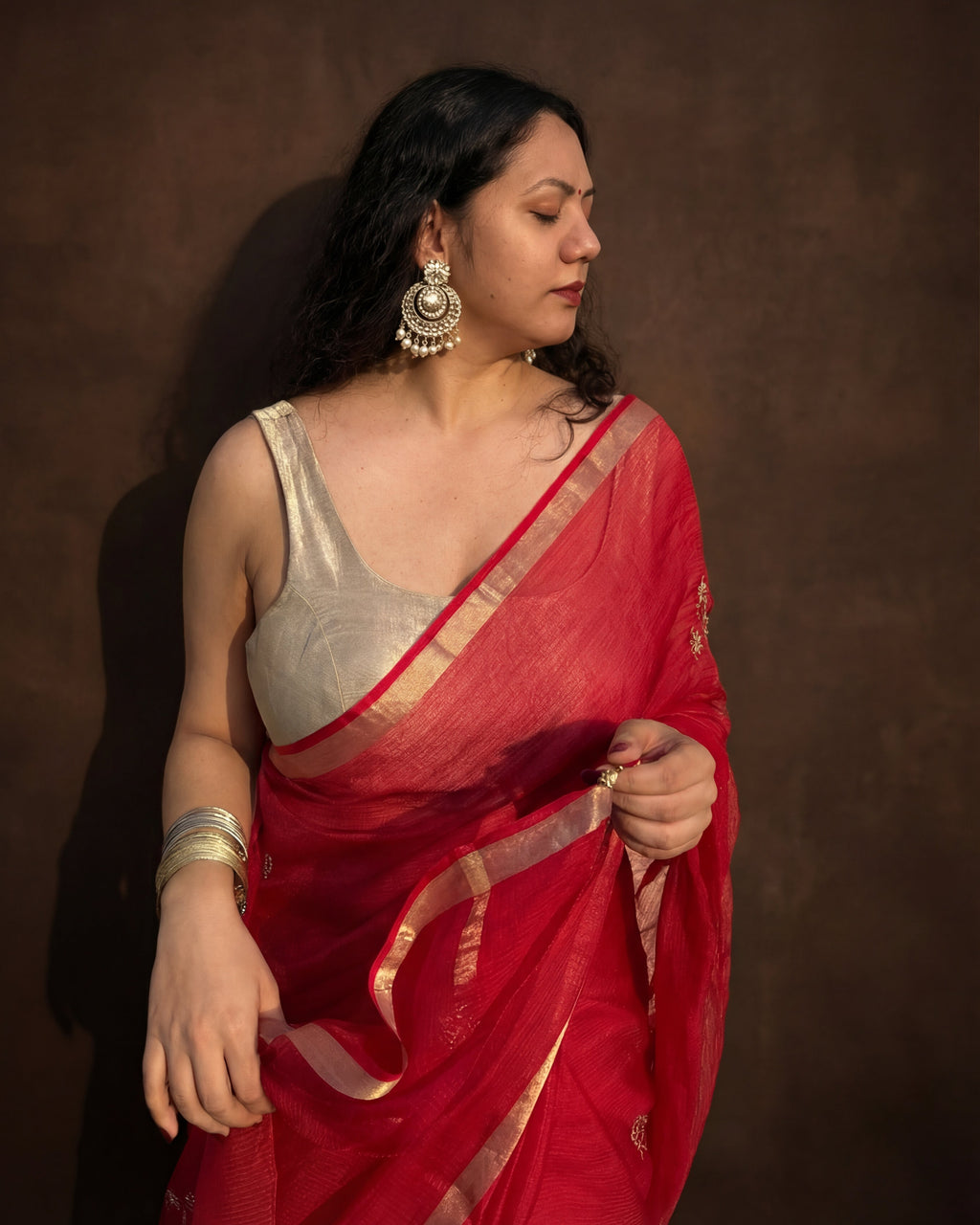 Woman wearing a red embroidered kota silk saree with a gold border against a brown background